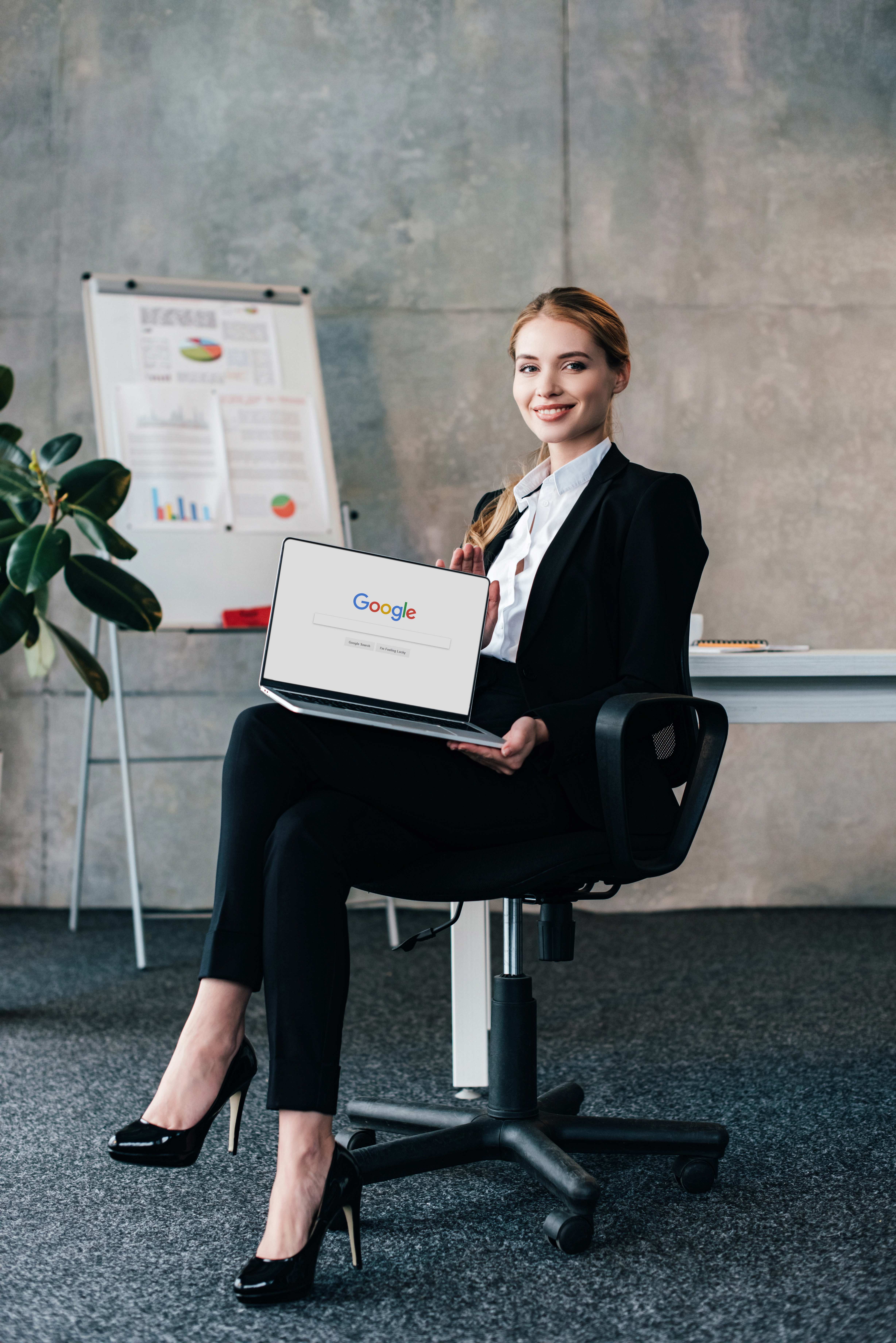 pretty smiling businesswoman sitting in chair and holding laptop with google on display